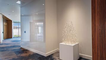 Un moderno vestíbulo de hotel con un separador de vidrio, una escultura blanca y una alfombra azul.