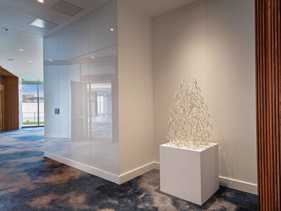 Un moderno vestíbulo de hotel con un separador de vidrio, una escultura blanca y una alfombra azul.