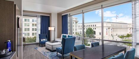 A hotel room with a large window, a dining table, and a sofa.