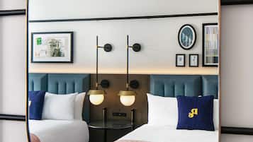 A hotel room with a large oval mirror reflecting the bed, bedside tables, and wall decor.
