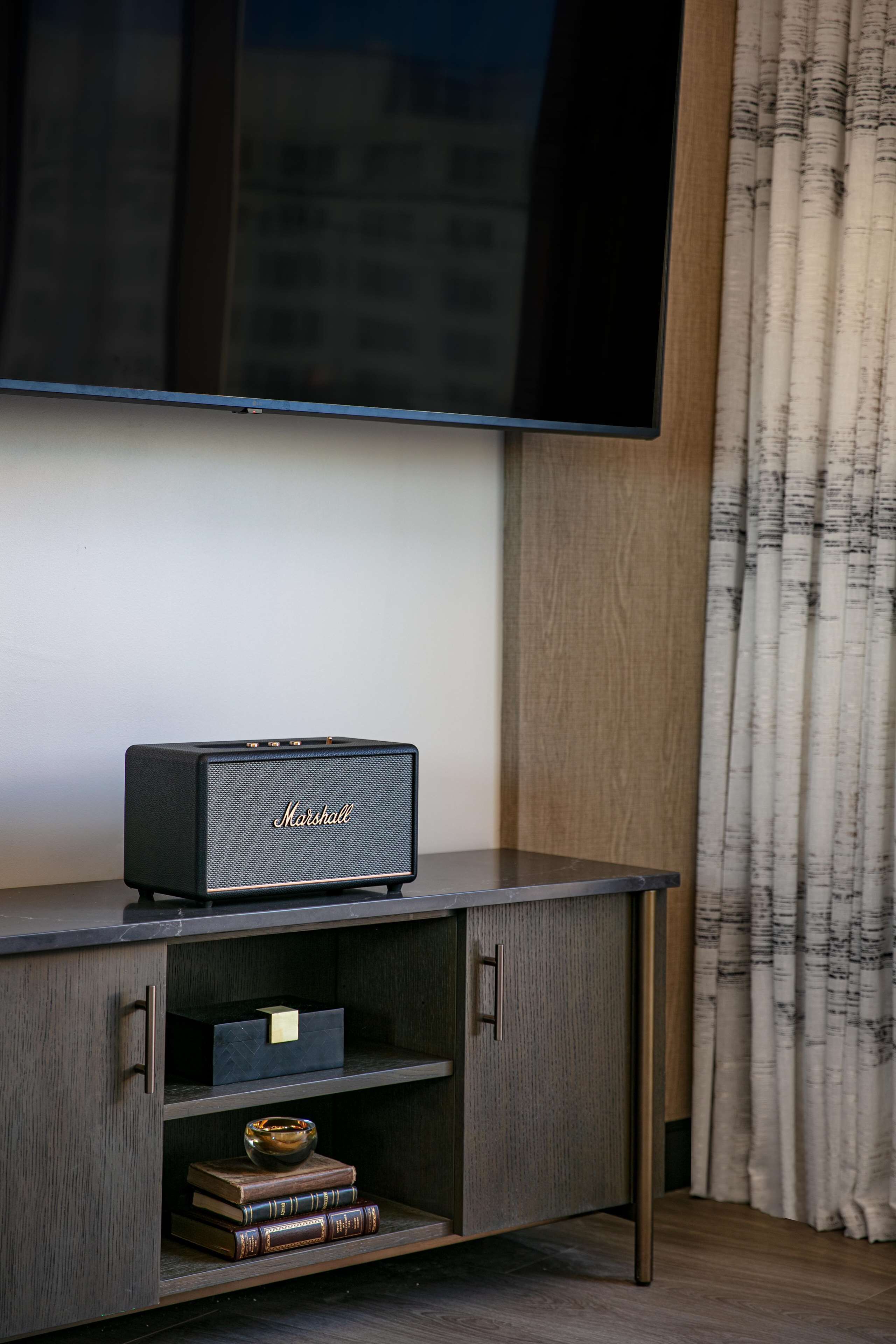 Un televisor de pantalla plana montado en una pared sobre un mueble de entretenimiento de madera con un altavoz Marshall.