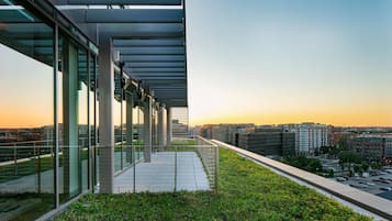 A rooftop terrace with a glass railing, offering a view of the cityscape at sunset.