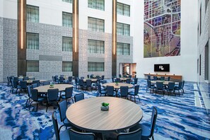 Une salle de conférence spacieuse, dotée de plusieurs tables et chaises, d’une grande fresque murale et d’un design moderne avec des luminaires verticaux.