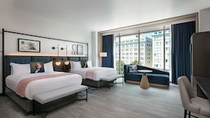 Una habitación de hotel moderna con dos camas, un sofá, una mesita y un ventanal con vistas a la ciudad.