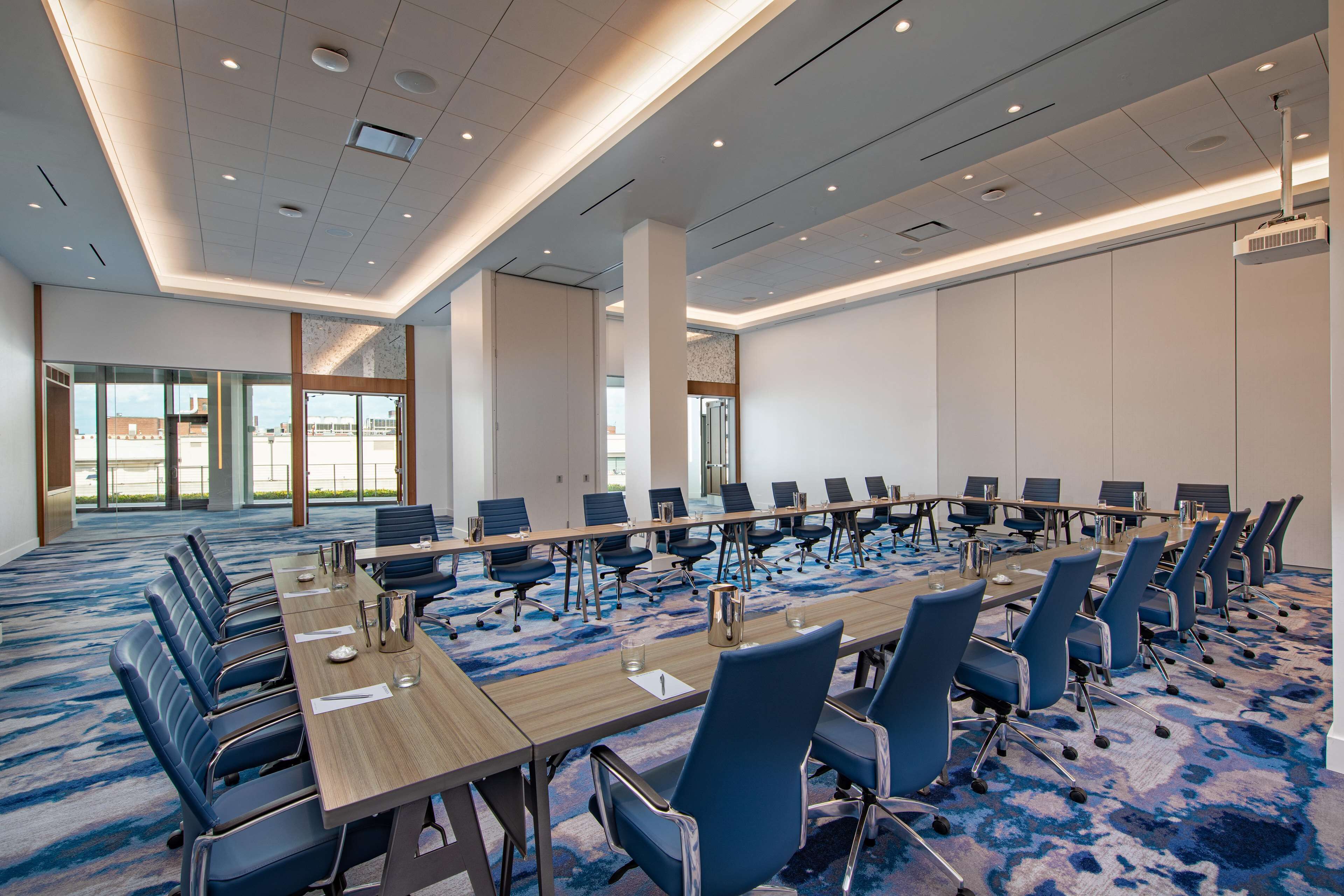 A conference room with a long table, blue chairs, and a carpeted floor.