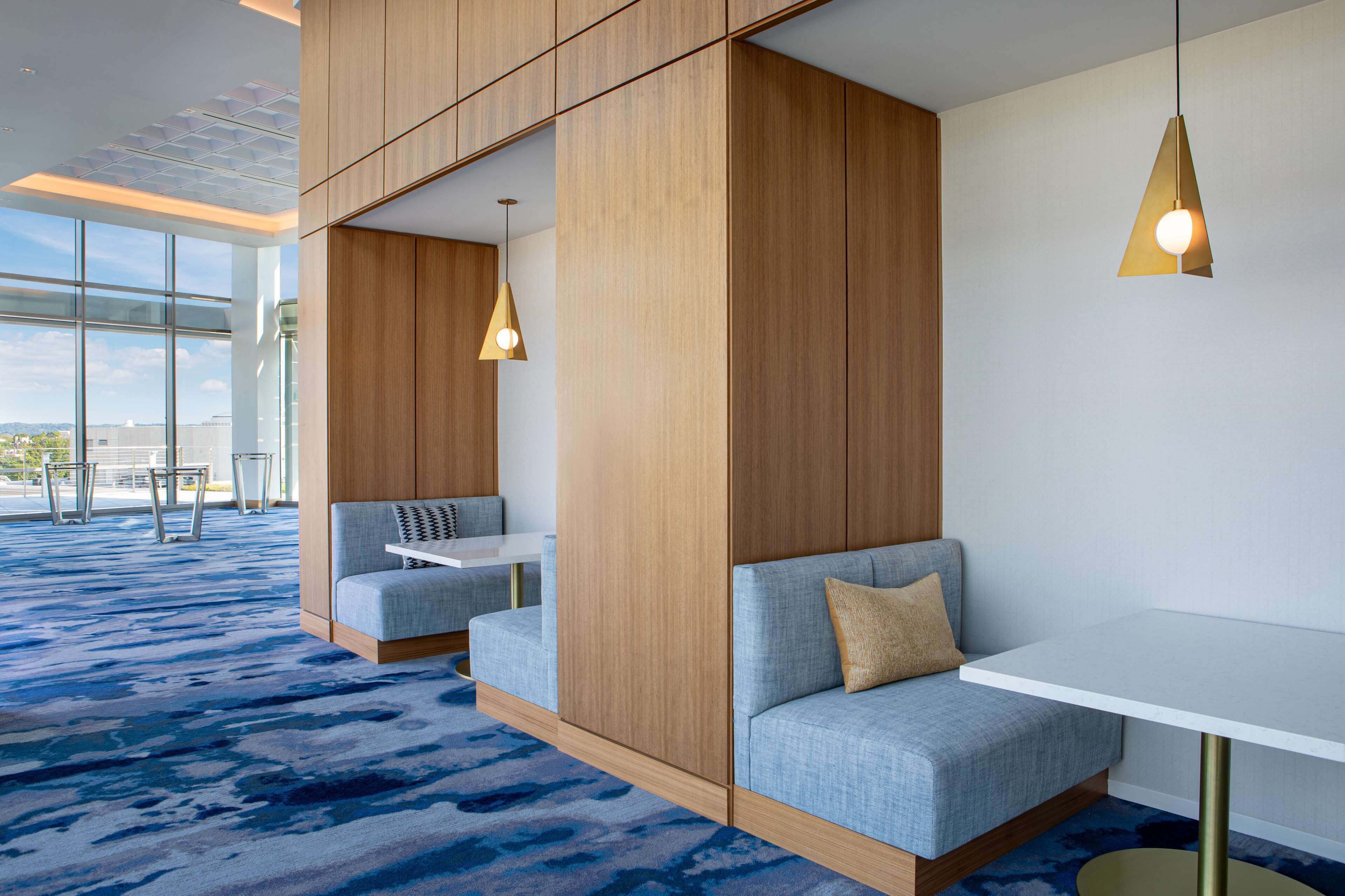 A modern hotel room with a large window, a blue carpet, a white table, and a blue sofa with a gold lamp.