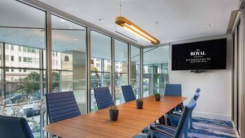 A conference room with a long table, blue chairs, and potted plants.