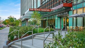 Una entrada de hotel moderna con fachada de vidrio, asientos exteriores y una escalera que lleva a la entrada.