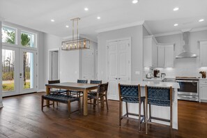 A spacious kitchen with white cabinetry, a stainless steel range hood, and a dining area with a wooden table and chairs. - ☀️Bright & Open-Private Fenced in Yard-Bikes-Viva La Vida (Santa Rosa Beach)