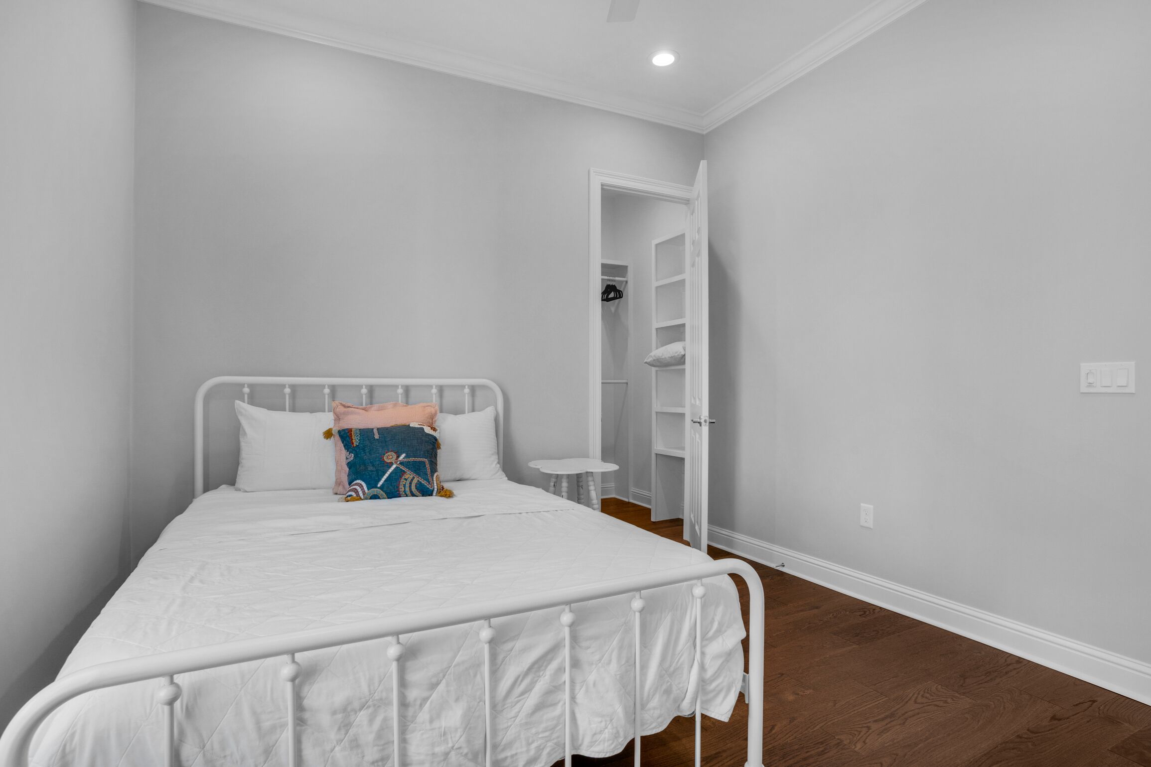 A bedroom with a white metal bed frame, a white mattress, and a small bedside table.