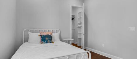 A bedroom with a white metal bed frame, a white mattress, and a small bedside table.