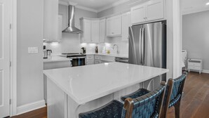 A modern kitchen with white cabinetry, a stainless steel refrigerator, and a central island with seating. - ☀️Bright & Open-Private Fenced in Yard-Bikes-Viva La Vida (Santa Rosa Beach)