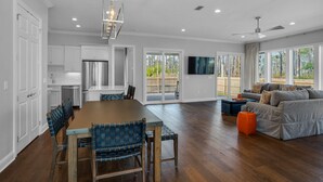 A spacious kitchen with white cabinets, a large wooden dining table, and blue chairs. There is a sliding glass door leading to a patio area with a gray sofa and orange ottoman. - ☀️Bright & Open-Private Fenced in Yard-Bikes-Viva La Vida (Santa Rosa Beach)