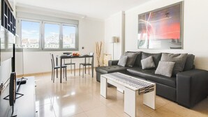 A modern living room with a black leather sofa, a white coffee table, and a dining area with a table and chairs.