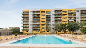 A hotel with a swimming pool surrounded by sun loungers and palm trees.