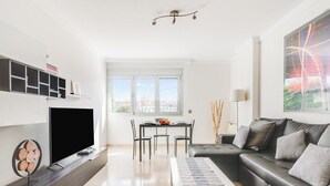 A modern living room with a flat-screen TV, a sofa, a coffee table, and a dining area with chairs and a table.