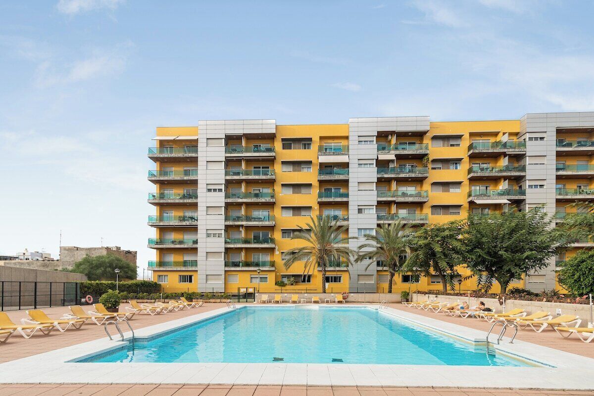 A hotel with a swimming pool, multiple balconies, and a clear sky.