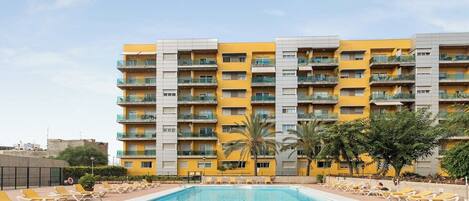 A hotel with a swimming pool, multiple balconies, and a clear sky.
