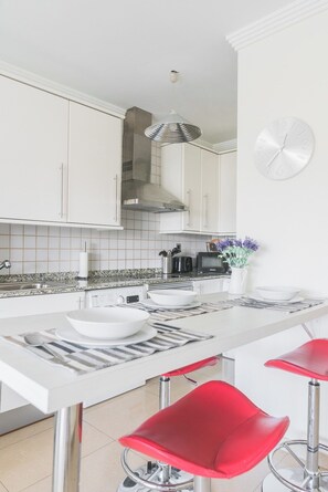 A modern kitchen with white cabinets, a stainless steel range hood, a microwave, and a dining area with a white table and red chairs.