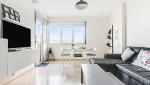 Ein modernes Wohnzimmer mit Flachbildfernseher, einer Couch, einem Esstisch mit Stühlen und einem großen Fenster mit Blick auf die Stadt.