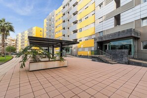 A multi-story residential building with balconies, a covered outdoor area, and a staircase leading to the entrance.