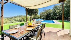 Un espace de restauration en plein air avec une table dressée pour un repas, offrant une vue sur une piscine et une végétation luxuriante.