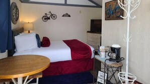 A bedroom with a bed, a table, a lamp, a bicycle wall decoration, and a coat rack. - Cabin 21 - Bicycle Retreat (Helena)