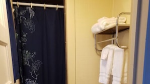 Un baño pequeño con inodoro, estante con toallas y cortina de ducha estampada con motivos florales.