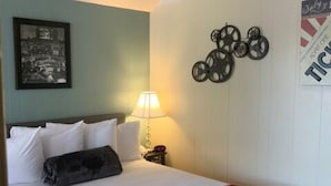Una habitación de hotel con cama, mesita de noche, lámpara, un cuadro enmarcado y un adorno en la pared.