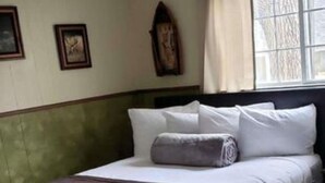 Una cama bien hecha con cabecera oscura, ropa de cama blanca y una toalla enrollada. Hay cuadros en la pared y una ventana con cortinas.