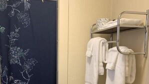 Un baño con cortina de ducha con motivos florales, un perchero con toallas dobladas y un inodoro blanco.