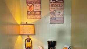 Una habitación pequeña con tocador, cafetera y microondas. Hay dos letreros en la pared con motivos de caza y pesca.