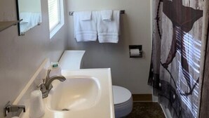 A bathroom with a white sink, a toilet, and a shower curtain with a rustic design. - Cabin 26 - Coyboy Corner (Helena)