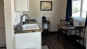 A compact kitchen with a sink, stove, and a dining area with a table and chairs. - Cabin 26 - Coyboy Corner (Helena)