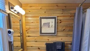 Un baño pequeño con paneles de madera, un lavabo, un inodoro, una cortina de ducha y un cuadro en la pared.