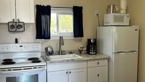 Une cuisine de taille réduite avec des meubles blancs, une cuisinière, un évier et un réfrigérateur.