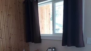 Un coin repas avec une table et des chaises en bois, une fenêtre avec des rideaux et une vue sur une clôture en bois à l’extérieur.