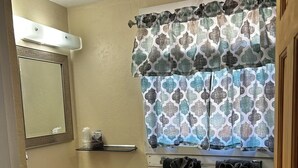 Baño con lavamanos, espejo y ventana con cortinas estampadas.