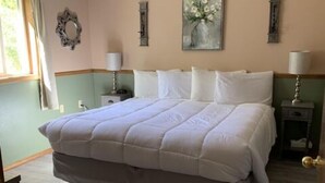 A bedroom with a large bed, two bedside tables, a wall-mounted lamp, and a window with curtains. - Suite 32 - King Suite (Helena)