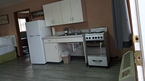 A compact kitchen with white cabinets, a refrigerator, a stove, and a sink. - Suite 32 - King Suite (Helena)