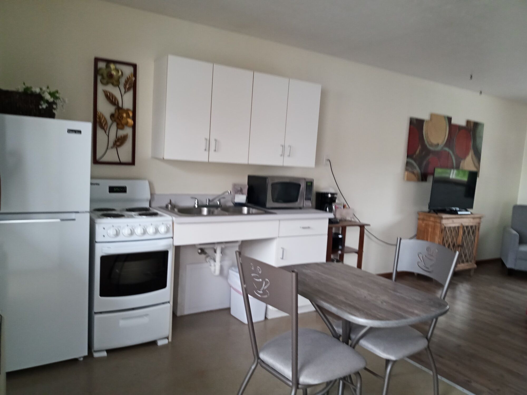 A compact kitchen with white cabinets, a stove, microwave, and a dining area with a table and chairs.