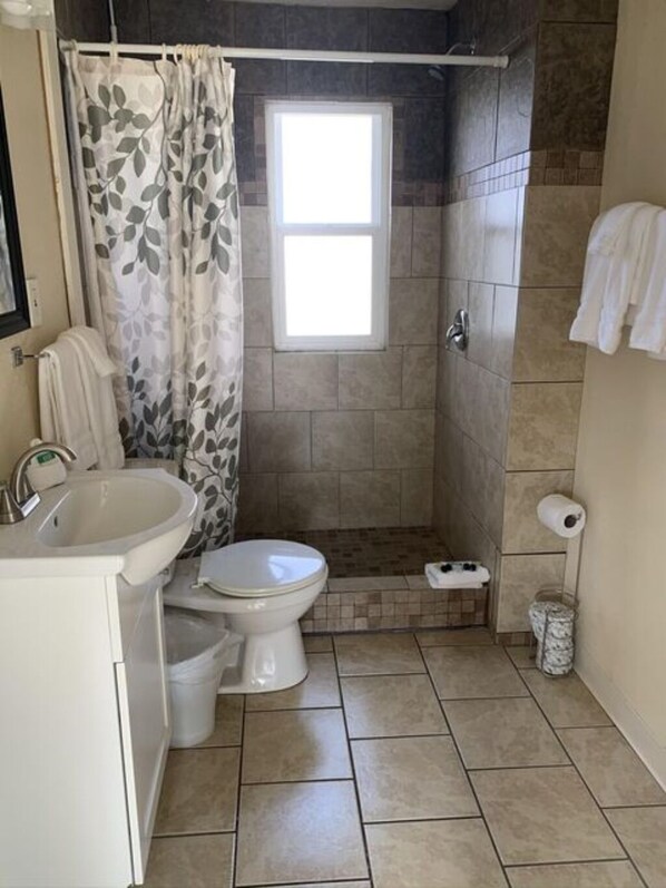 Et badeværelse med brusebad, toilet, håndvask og et vindue.