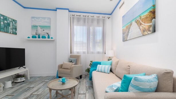 Sala de estar com televisão, sofá, poltrona e um quadro com uma cena de praia.