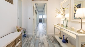 Um corredor com piso de madeira, um console branco com uma luminária e um espelho.