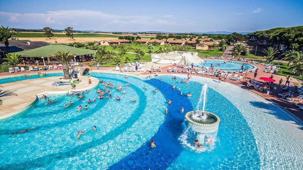 Una gran piscina al aire libre con múltiples carriles, un tobogán acuático y una zona circundante con tumbonas y sombrillas.