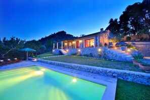 Casa de piedra con piscina, mobiliario exterior y una escalera de piedra que conduce a la entrada.