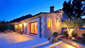 A stone house with a patio, a dining area, and a well-lit entrance. - La Salve d'alt villa with private pool (Pollensa)