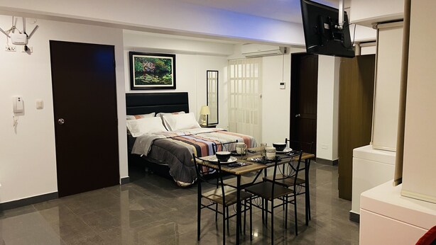 Ein Hotelzimmer mit Bett, Esstisch mit Stühlen, einem an der Wand befestigten Fernseher und einem Fenster mit Vorhängen.