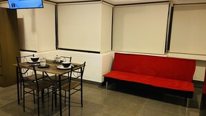 Ein Zimmer mit Esstisch, gedecktem für vier Personen, einem roten Sofa und einem an der Wand befestigten Fernseher.