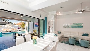 Un salon moderne avec vue sur la piscine, un canapé blanc et un coin repas comprenant une table et des chaises.